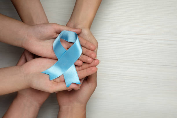 istock People holding light blue awareness ribbon at white wooden table, top view. Space for text 1406181427