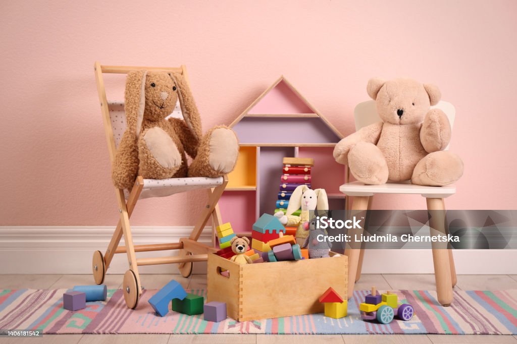 Set of different cute toys on floor near pink wall Dollhouse Stock Photo