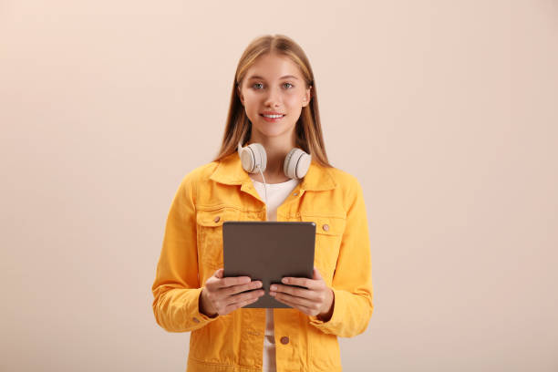 nastoletni uczeń z tabletem i słuchawkami na beżowym tle - neutral look audio zdjęcia i obrazy z banku zdjęć