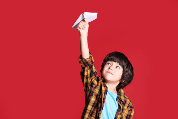 istock Cute little boy with paper plane on red background 1406182146