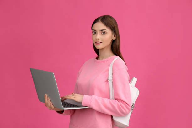 istock Teenage student with laptop and backpack on pink background 1406183103
