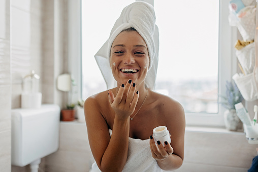 One woman, beautiful young woman sitting on sofa in living room and woman applying face cream on her face