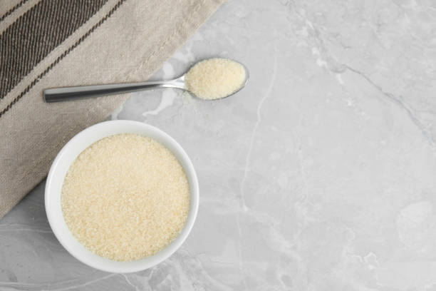 istock Gelatin powder in bowl and spoon on light grey marble table, flat lay. Space for text 1406183509