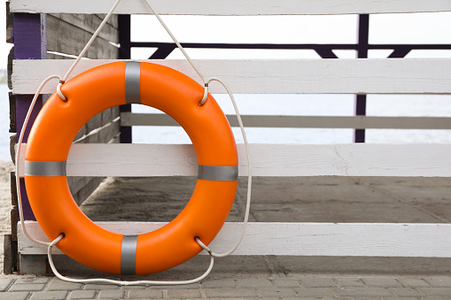 Orange life buoy hanging on white wooden fence at beach, space for text