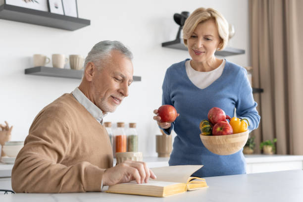 istock Middle aged man reading book to his wife on kitchen 1406187096