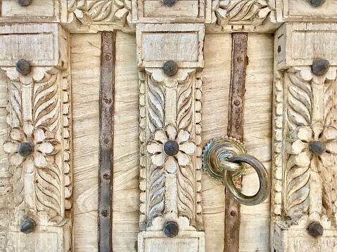 Horizontal close up of rustic wood front door with carved flower and designs with brass door knocker