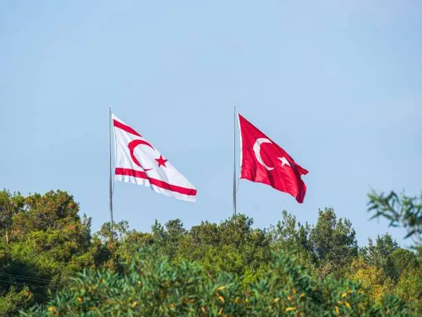 Large Turkish and Northern Cypriot flags flying side by side on a sunny afternoon near Girne, TRNC
