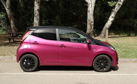 Grado, Italy. June 27, 2022. Side view of bright purple Toyota Aygo with a public park on background.