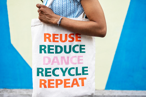 Close up of a a fabric shopping bag on the light blue wall. Bag has a message Reuse, Reduce, Dance, Recycle, Repeat