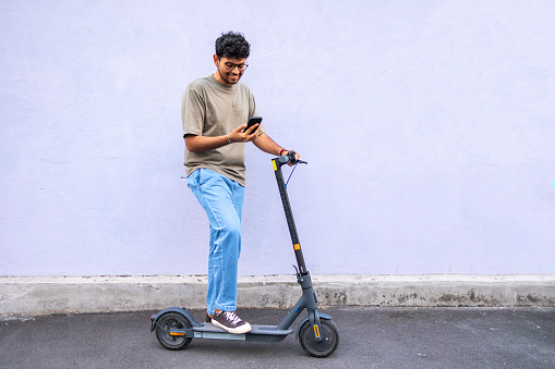 Indian man riding a electric scooter. He is using his mobile phone while making a break