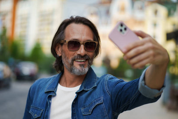 istock Middle aged handsome grey bearded metrosexual man smiling on camera old town wearing casual. Happy senior man on street of european city making selfie using mobile phone. Travel concept 1406201935