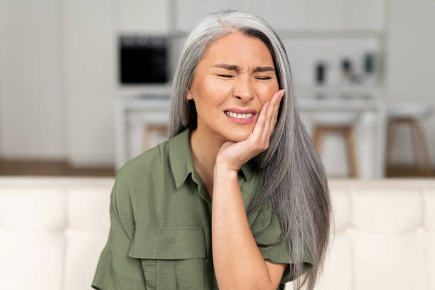 Troubled mature 50s woman with gray-hair feels strong toothache Troubled mature 50s woman with gray-hair feels strong toothache, holding cheek and suffering from strong dental pain sitting on sofa, middle-aged female undergoing tooth pain, enamel sensitivity toothache stock pictures, royalty-free photos & images