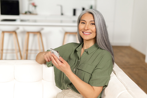 Contemporary senior woman spends time with a smartphone, mature woman scrolling news feed on the mobile phone, texting online with friends or children, enjoying messaging in social networks