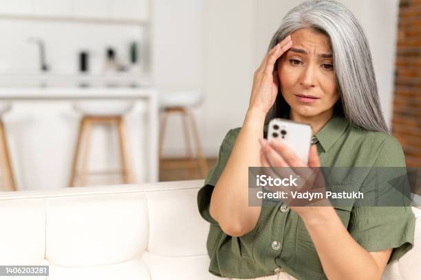 Frustrated Unhappy Grayhaired Mature Woman Sitting On Sofa Holding Smartphone Senior Female Has Not Enough Money For Online Transaction Stock Photo - Download Image Now