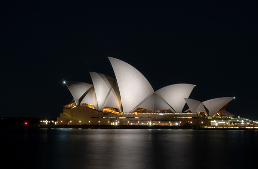 Sydney Australia - August 6, 2017: Night-time in Sydney, and the brightly-illuminated shape of the city's Opera House seems to glow in the darkness.