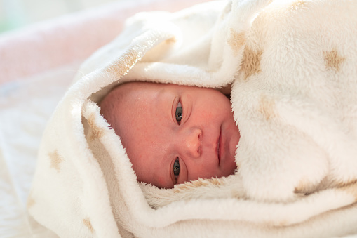 portrait of a newborn baby lying in his crib wrapped in a soft white blanket with stars ready to go to sleep