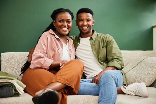 istock Young couple smiling while sitting together on a sofa at home 1406207857