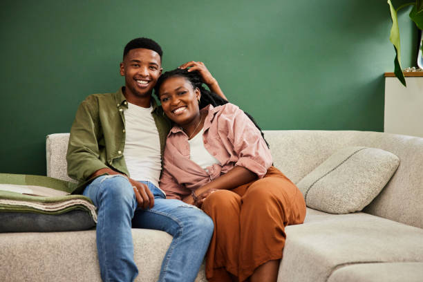 istock Young couple smiling while sitting together on a sofa at home 1406207943