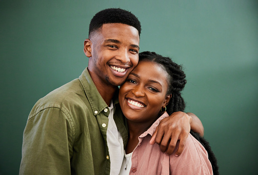 Portrait of smiling young African couple standing arm in arm together in front of a green wall in their stylish living room at home