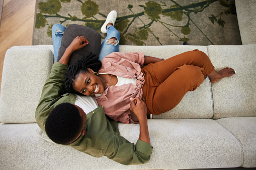High angle view of a smiling young African woman lying on her boyfriend's lap while relaxing on their living room sofa at home