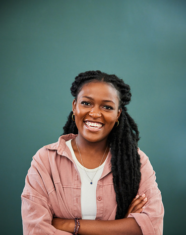 Portrait of a young African woman with long dreaded hair laughing while standing with her arms crossed in front of a green wall