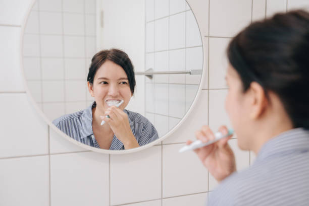 Asian Woman Cleaning Teeth With Toothbrush In Bathroom, Asian Woman Cleaning Teeth With Toothbrush And Paste Doing Daily Oral Hygiene Routine In Bathroom At Home. Closeup Of Female Brushing Teeth. asian brushing teeth morning routine stock pictures, royalty-free photos & images