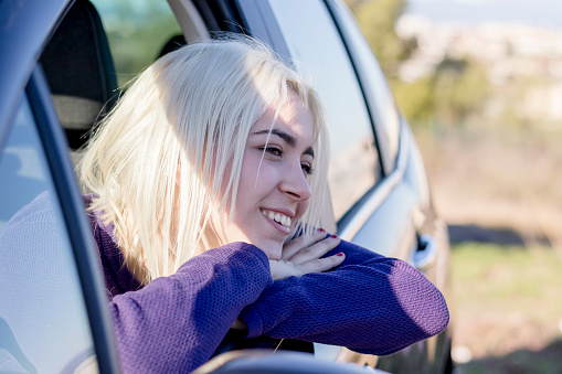 Smiling young woman looks out of a car window