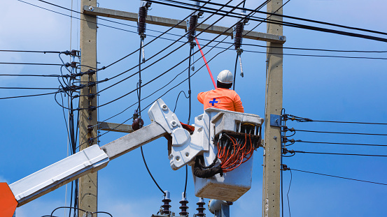 Low angle view of electrician with disconnect stick tool on crane truck are working to install electrical transmission on power pole against blue sky