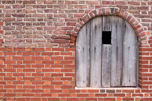 A arched wooden window is surrounded by old red brinks