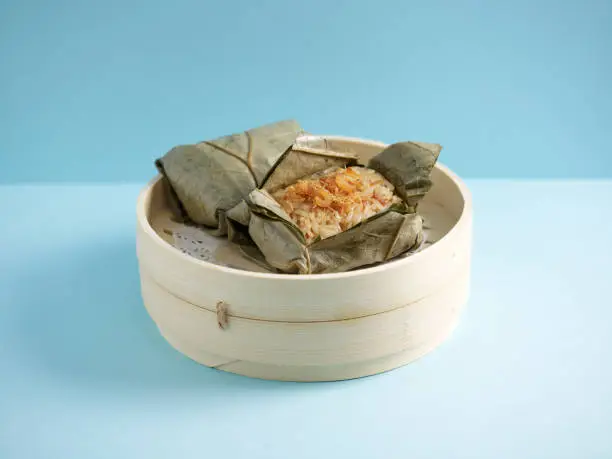 Steamed Glutinous Rice with Chicken Wrapped in Lotus Leaf served in a wooden bowl with chopsticks isolated on mat side view on grey marble background
