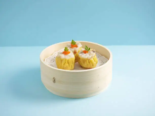 Photo of Steamed Pork Dumpling Siew Mai served in a wooden bowl with chopsticks isolated on mat side view on grey marble background