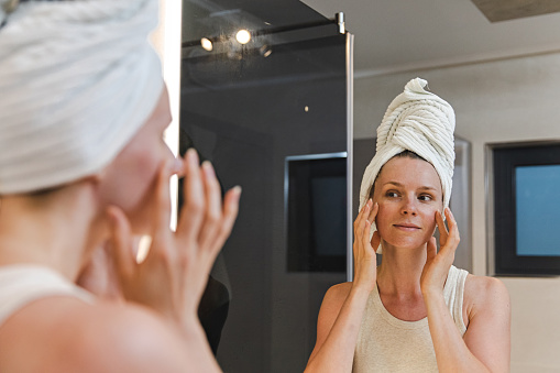 Woman applying face cream in front of a mirror