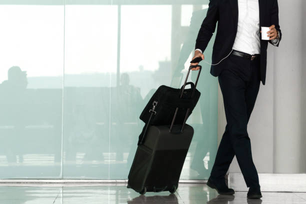 istock Unrecognizable businessman walking with his suitcase through the airport while holding a coffee in his hand. 1406221011
