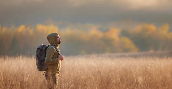 Young handsome man posing in autumn nature. guy standing in field over sunset. Goals, hopes and aspirations concept. enjoying nature view. Hiking and trekking. Concept Adventure and Travel