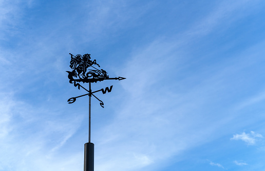 Weather vane showing direction of wind against clear blue sky. Metal weather vane with rider silhouette.