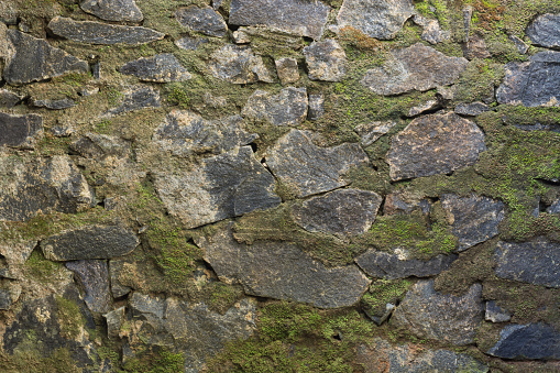 section of a stone wall surface built with cement and covered with green moss, closeup of retaining wall background abstract