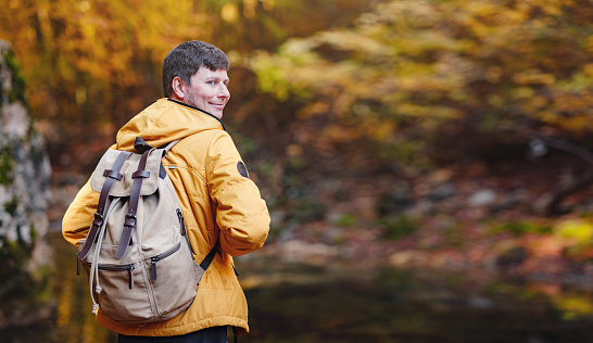 Travel and road trip concept at autumn. Adventure and active lifestyle in nature. Tourist hiking in forest. Caucasian man in yellow jacket walks in woods.