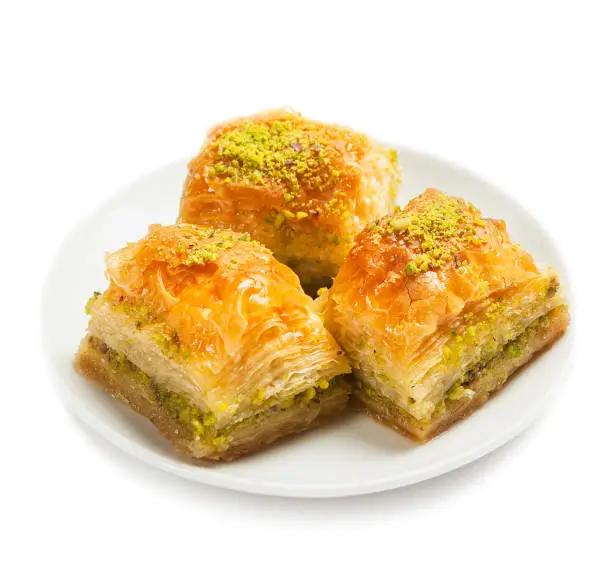Photo of baklava with pistachios, 3 pieces, on a white plate, isolated, side view