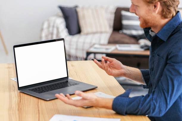 istock Caucasian young man freelancer or business owner working remotely, communicates online using video call sitting at workplace looking at mockup empty screen, discussing something 1406229531