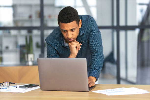 istock Concentrated Afro man working using laptop in modern office. Successful business African American man, looking at computer screen, analyzing something 1406229555