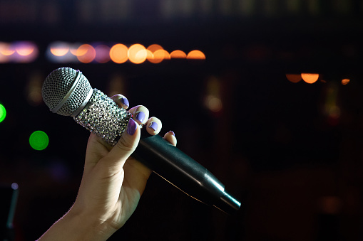 Close-up of woman hand holding microphone on stage, copy space.