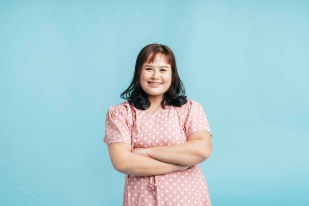 Portrait Confidence cheerful beautiful  Asian woman plus size happy smile in pink pastel dress cross arm on isolate light blue studio background. stock photo