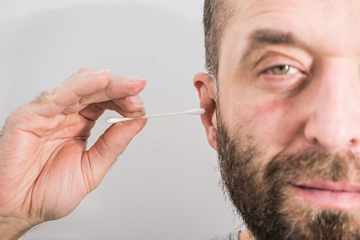 Man about to clean his ears using Q-tip cotton swab. Hygiene essentials concept. Removing wax from ear.