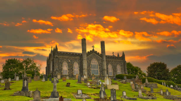 st. john rc roman catholic chapel churchyard cemetery, coleraine, londonderry o zachodzie słońca z dramatycznym pomarańczowym i żółtym kolorem nieba z chmurami w tle i nagrobkami na pierwszym planie - coleraine zdjęcia i obrazy z banku zdjęć