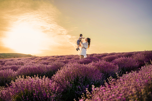 Happy mother and son walking through lavender field at sunset