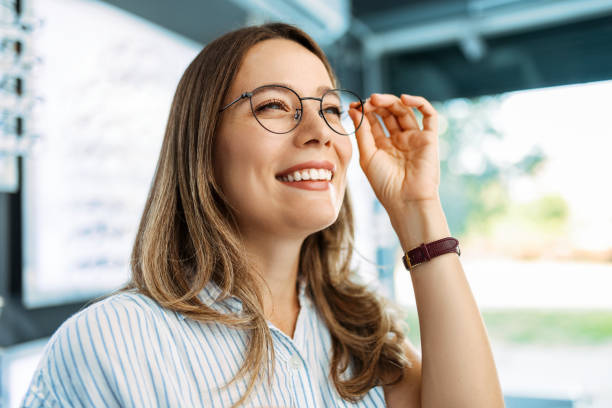 眼鏡店で眼鏡を選ぶ笑顔の若い女性 - optics store ストックフォトと画像