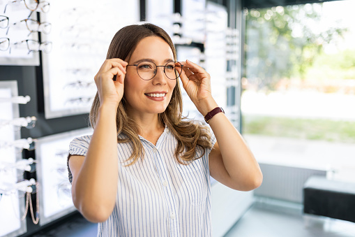 Fashionable woman choosing eyeglasses in modern optical store