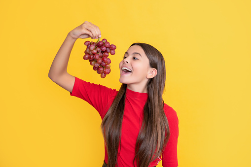 glad amazed kid hold bunch of grapes on yellow background.