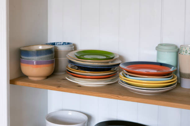 istock Wooden shelf with kitchen utensils, rustic style. Tableware, plates and bowls stand on a shelf in the kitchen. Cupboard with set of colourful dishes, modern interior. 1406235037