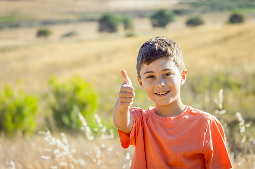 An 11 year old boy is standing in a country field giving a thumbs up. Photos taken on Lemnos island in Greece.